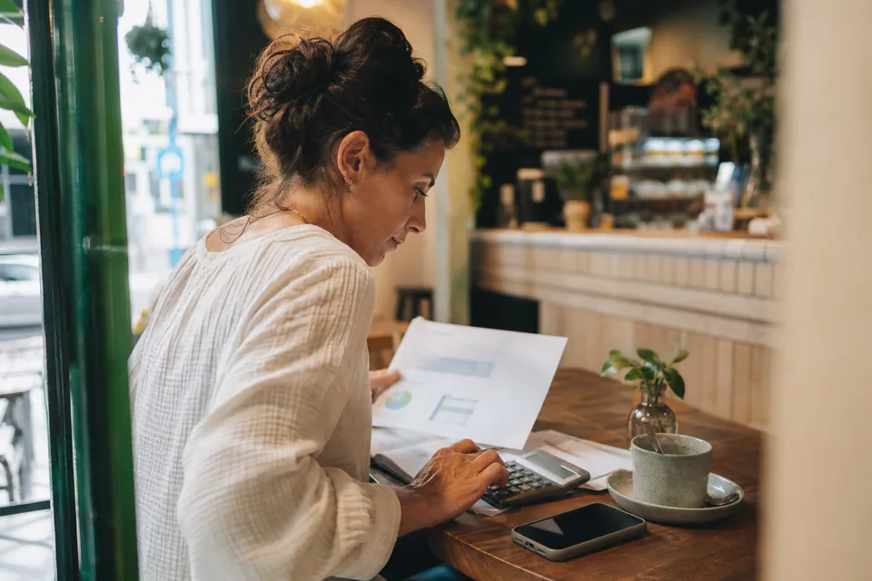 Small business owner reviewing a monthly software budget with a calculator and phone