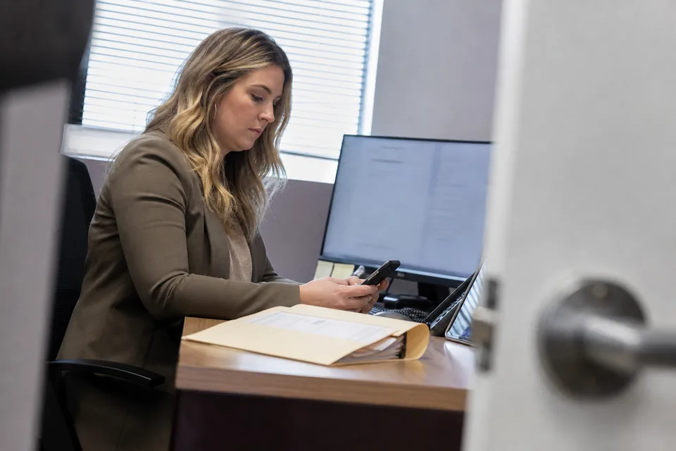 Mortgage loan officer texting a borrower from her desk next to a loan file
